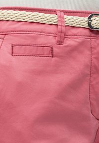 Zbliżenie na różową talię spodni z przewleczonym białym plecionym paskiem przez szlufki i wszytą tylną kieszenią.