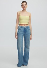 Top corto amarillo claro con tirantes finos, combinado con pantalones vaqueros azules de tiro alto y pierna ancha, con lavado descolorido y bolsillos delanteros.
