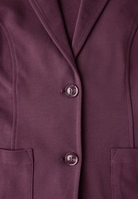 Paarse blazer van gladde stof, voorzien van twee knopen, spitse revers en twee voorzakken. De knoop heeft een decoratief ontwerp.