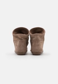 Un par de botas de tobillo de ante marrón con tacones bajos y planos, mostradas desde la parte trasera sobre un fondo blanco.