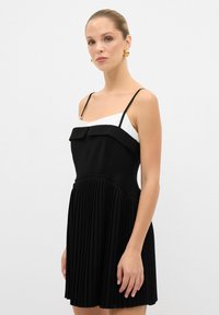 Czarna i biała sukienka bez rękawów z dopasowanym topem i plisowanym dołem. Posiada cienkie ramiączka oraz falbaniasty dekolt. Gładka tekstura, elegancki design.