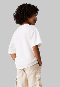 T-shirt bianco a maniche corte in cotone, con vestibilità rilassata e colletto rotondo classico, abbinato a pantaloni cargo beige chiaro.