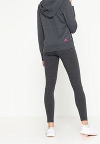 Grijze hoodie en bijpassende leggings met een roze Adidas-logo, met een gladde textuur en een aansluitend ontwerp. Witte sportschoenen vervolledigen de outfit.
