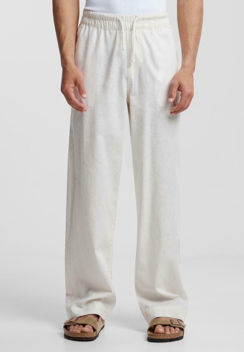 Linnebyxor i ljus krämfärg med elastisk midja och avslappnad passform, med en slät textur och vida ben. Sandaler på fötterna.