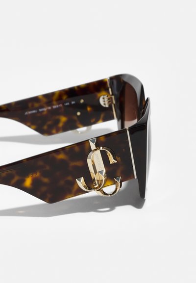 Tortoiseshell sunglasses featuring a wide frame and gold logo accent on the temple. The lenses are dark with a smooth texture.