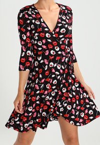 Floral wrap dress in black fabric, featuring red, pink, and white flowers. Three-quarter sleeves and flared skirt with ruffled hem.