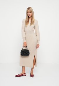 Abito lavorato a maglia beige con maniche lunghe e uno spacco frontale, abbinato a ballerine rosse e a una borsa nera texture. Design semplice ed elegante.