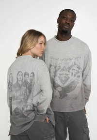 Szary longsleeve z długim rękawem, z nadrukami z przodu i z tyłu. Z tyłu znajdują się szczegółowe ilustracje ludzi i natury; z przodu znajdują się wzory z orłem i wilkiem.