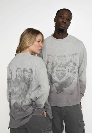 Sivý dlhý rukáv tričko s tlačou na prednej a zadnej strane. Zadná strana obsahuje podrobné ilustrácie ľudí a prírody; predná strana má dizajny orla a vlka.