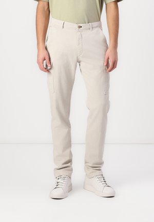 Beige cargobroek met zijzakken, gemaakt van katoen. Tapered fit, lichtgewicht stof en een knoopsluiting. Draagt met witte sneakers.