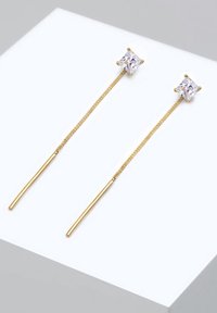 Pendientes de tono dorado con un diseño de palo largo y una gema cuadrada y transparente en la parte superior. El metal tiene un acabado suave y una textura delicada.