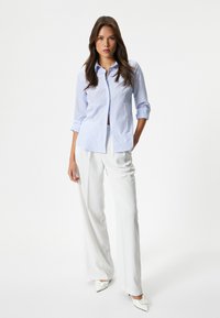 Camicia a righe blu chiaro con bottoni, maniche lunghe arrotolate, abbinata a pantaloni bianchi a gamba larga e tacchi bianchi a punta.
