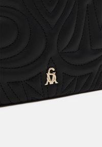 Sac en cuir noir avec des motifs ondulés en relief, un accent logo en métal doré et des coutures contrastantes pour ajouter de la texture et du détail.
