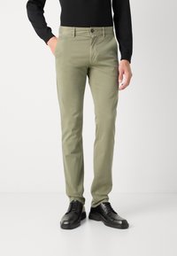 Khaki chinos med slim fit, tillverkade av bomull, med knappknäppning och bälteshällor, tillsammans med svarta läderskor.