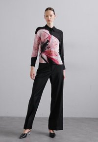 Camicia button-up con motivo floreale rosa da un lato e tessuto nero dall'altro, abbinata a pantaloni larghi neri e scarpe a punta.