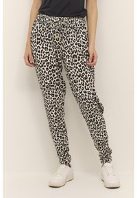Joggingbroek met luipaardprint van zachte stof, met een elastische tailleband met trekkoord, aansluitende boorden en zijzakken. Witte sneakers te zien.
