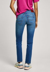 Kitsad sinised teksapüksid tagakottide ja õmblusdetailidega, kombineeritud erksa roosa särgiga ja mitmevärviliste tossudega.