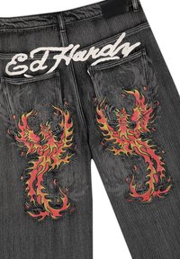 Schwarze Denim-Jeans mit roten und gelben flammenden Phönix-Designs auf den Gesäßtaschen und weißem "Ed Hardy" Schriftzug über den Taschen.