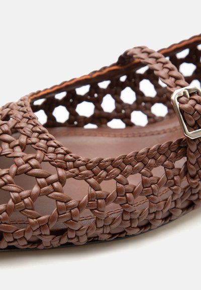 Pruun punutud nahast sandaal pannaliga rihma ja tihedalt põimitud avatud mustriga lame tallaga.