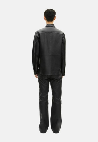 Giacca e pantaloni in pelle nera, con una vestibilità strutturata, dettagli sulle cuciture e una texture liscia, visti dal retro.