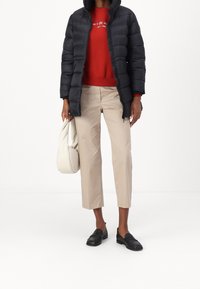 Person wearing black puffer jacket, red sweater with white text, beige cropped pants, black loafers, holding a light beige handbag.