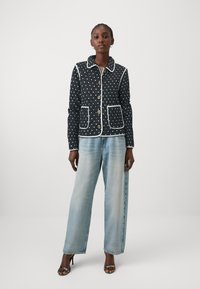 Quilted marineblå jakke med hvite polkadotter, kontrasterende hvit trim og lapper; satt sammen med lyseblå vide bukser og høyhælede sko.