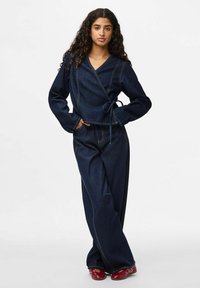 Top avvolgente in denim scuro con maniche lunghe, abbinato a pantaloni larghi coordinati. Presenta cuciture a contrasto e una cintura annodata in vita.