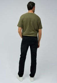 Camiseta de rayas en verde oliva para hombre, vaqueros negros y zapatillas blancas. La camiseta tiene mangas cortas y un corte holgado.