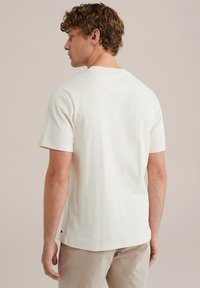 V-kaklo, trumpomis rankovėmis megztinis kremine spalva, su tekstūriniu, raukšlių dizainu ir vertikaliais raštais. Liemuo siauras, su šoniniu logotipo akcentu.