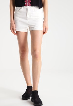 Kvinde iført hvide denimshorts med frynsede kanter, sorte net-ankelstøvler og en sort top med lyserød broderi.