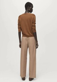 Bruine gebreide trui met lange mouwen, gecombineerd met beige broek met wijde pijpen. Gladde textuur en ontspannen silhouet. Effen achtergrond.