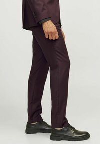 Pantalons ajustés bordeaux foncé avec une texture lisse, associés à des chaussures en cuir noires, à lacets et avec une semelle en caoutchouc.