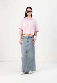 Lyserød cropped t-shirt med "Converse" logo, parret med en lang, lys blå denimnederdel og hvide slip-on sko. Sorte solbriller fuldender udseendet.