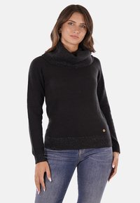 Maglione nero con collo a cowl, realizzato in un tessuto morbido e testurizzato, con dettagli lucidi all'orlo. Presenta maniche lunghe e un dettaglio circolare con logo in vita.