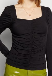 Maglietta nera a maniche lunghe con scollatura quadrata, caratterizzata da dettagli arricciati sul davanti e una silhouette aderente. Tessuto morbido ed elasticizzato.