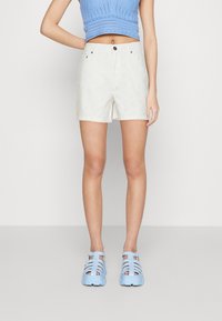 Shorts blancs avec un design en œillet et une fermeture à bouton ; associés à un haut en tricot bleu cropped et des sandales en jelly bleues.