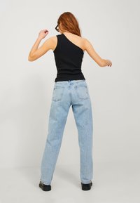 Top in tessuto nero a spalla unica con silhouette aderente, abbinato a jeans larghi blu chiaro e scarpe nere, visto da dietro.