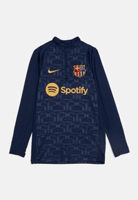 Marinblå långärmad fotbollsträningströja med subtilt mönstrad textur, med en gyllene Nike-logotyp, FC Barcelonas emblem och Spotify-logotyp.