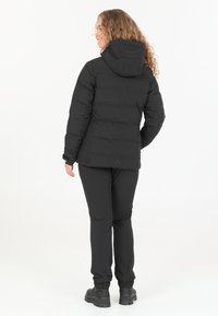 Schwarze Daunenjacke mit Kapuze, mit gestepptem Design. Kombiniert mit schwarzen Hosen und robusten schwarzen Stiefeln. Glatte Stoffstruktur.
