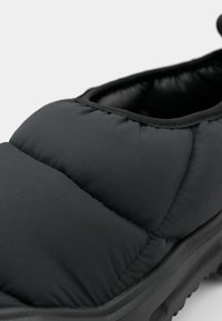 Black padded slip-on shoe with thick sole and stitched quilted details, designed for casual indoor or outdoor wear.