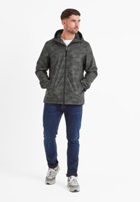 Dark green camouflage jacket with a zip front, adjustable hood, and a smooth finish. Paired with blue jeans and light gray sneakers.