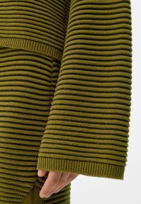 Pull en maille côtelée vert olive avec un motif texturé, des manches larges et une coupe ajustée avec une fente à l'ourlet.