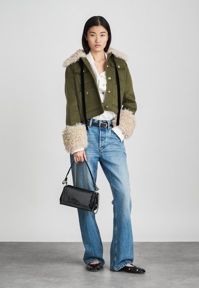 Casaco verde cortado com punhos bege felpudos, detalhes em botão preto, blusa branca, jeans azul claro e uma pequena bolsa preta com corrente.