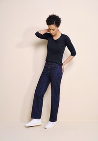 Musta pitkähihainen paita, joka on yhdistetty tummiin farkkucapriin, joissa on korkea vyötärö, suora lahkeensuuvaihtoehto, sekä valkoiset lenkkarit rentoa tyyliä varten.