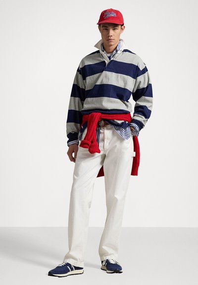 Collared rugby shirt in gray and navy stripes, red sweater tied at the waist, white pants, and navy athletic shoes. Red cap with logo.