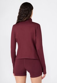 Bordeaux sportjack met lange mouwen en een hoge kraag, gemaakt van glad synthetisch materiaal. Ontworpen met een slim fit en zachte stiksels.