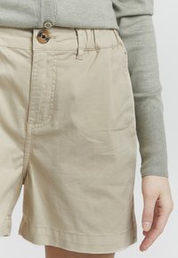 Beige shorts laget av bomull med en jevn tekstur, med en frontknapp, sidelommer og rett snitt i nederkant.