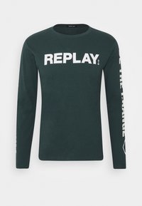 Dark green long-sleeve shirt with white "REPLAY" text on chest and partially visible text on right sleeve. Simple crew neck design.