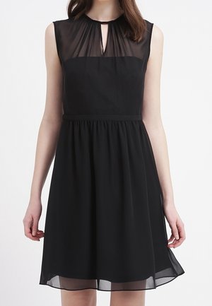 Schwarzes Kleid mit tailliertem Oberteil und ausgestellt Rock. Durchsichtige Überlagerung am Ausschnitt mit einem Schlüsselloch-Ausschnitt, geraffte Details an der Taille.