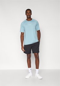 Αθλητική μπλούζα ανοιχτού γαλάζιου χρώματος με κοντά μανίκια, μαύρο σορτς, λευκές κάλτσες και λευκά αθλητικά παπούτσια. Διαθέτει το λογότυπο της μάρκας στο στήθος.